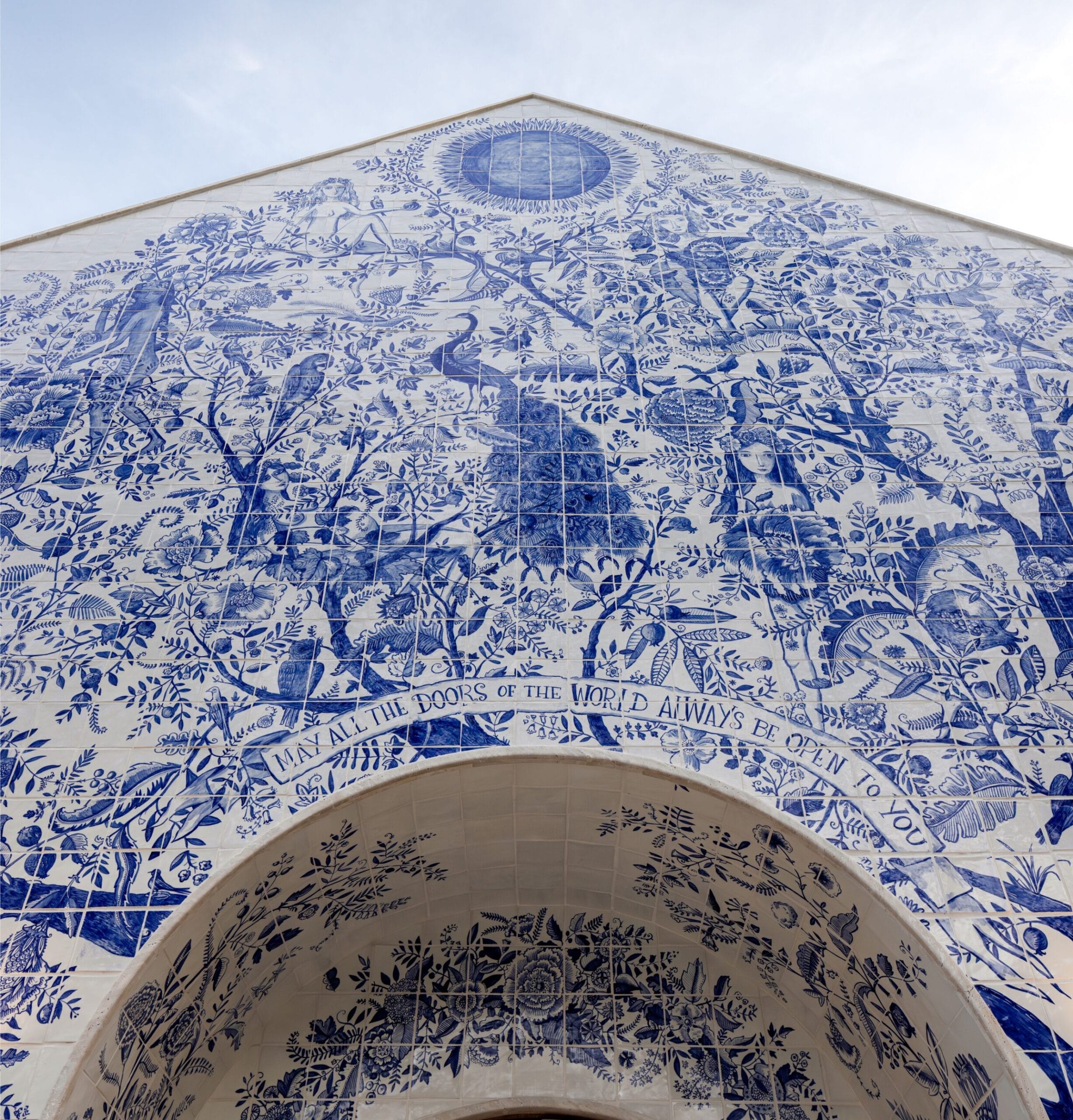 a detail of a shop facade completely covered in hand-painted blue tile featuring an elaborate tree of life motif with flowers and birds