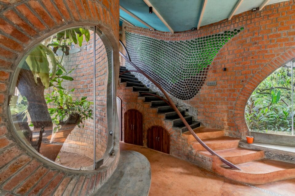 the view of a home's interior with a small staircase and large window revealing a tree. a wall of shimmering glass lines the staircase