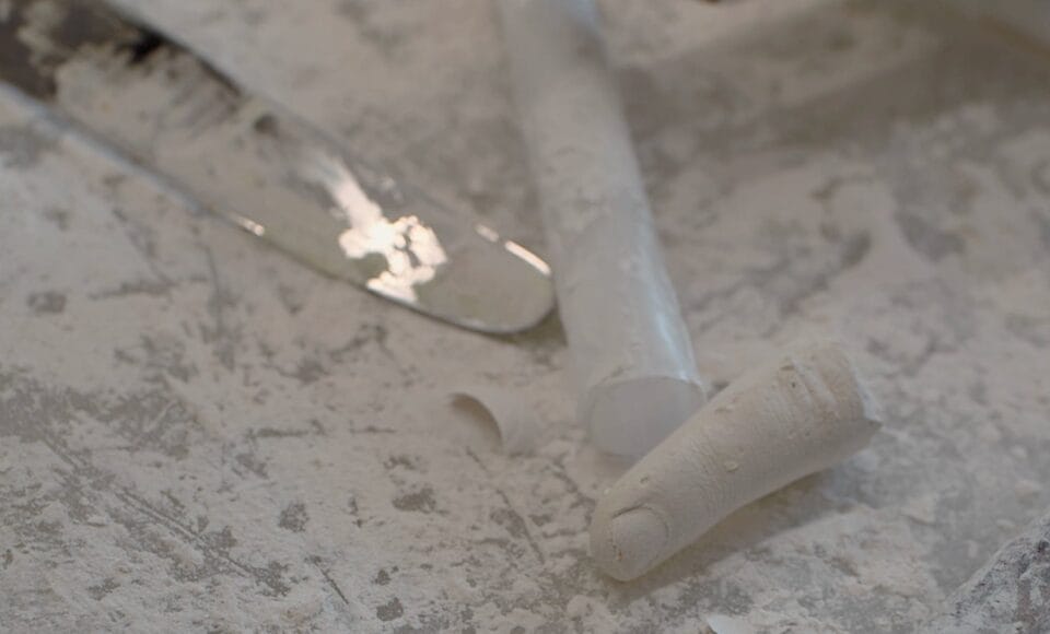 a video still of a white plaster finger on a table with tools and a knife