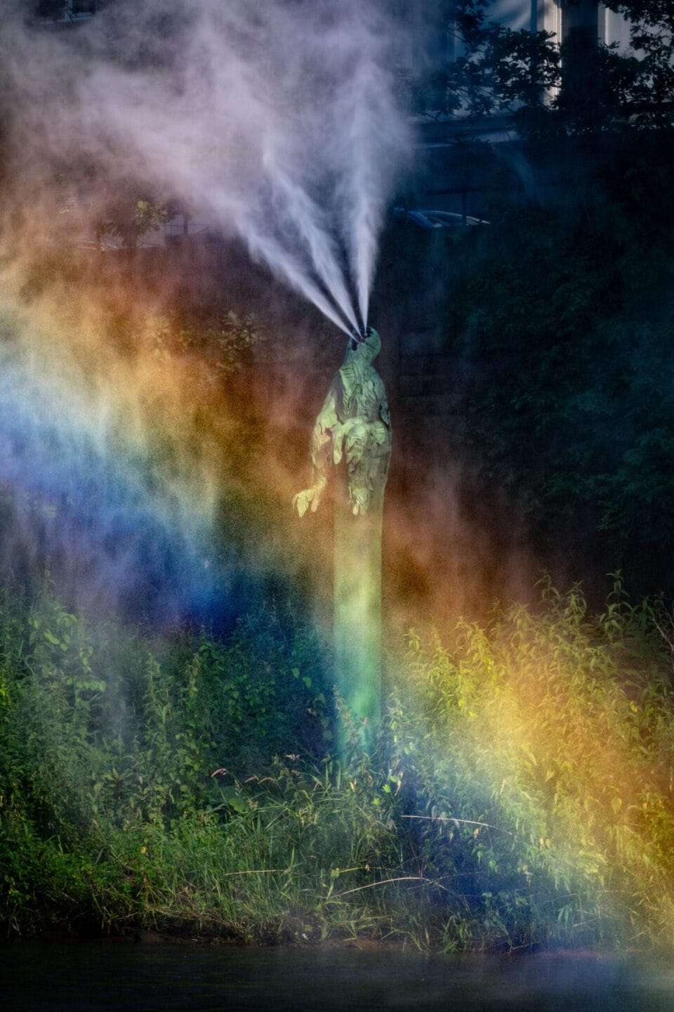 along a river, a fountain sprays water as a rainbow appears in front of it