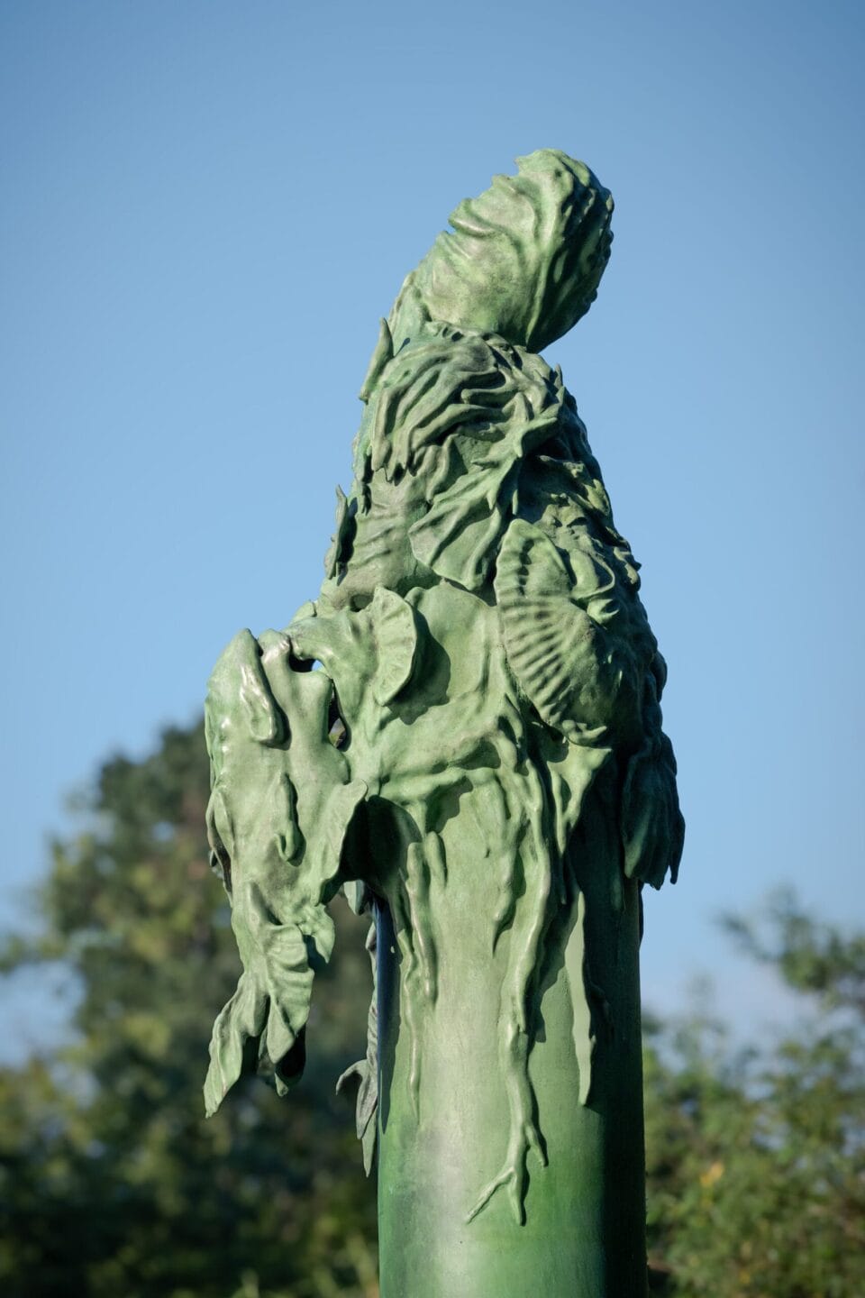 a tall fountain that resembles a sitting elf-like figure is situated next to a river