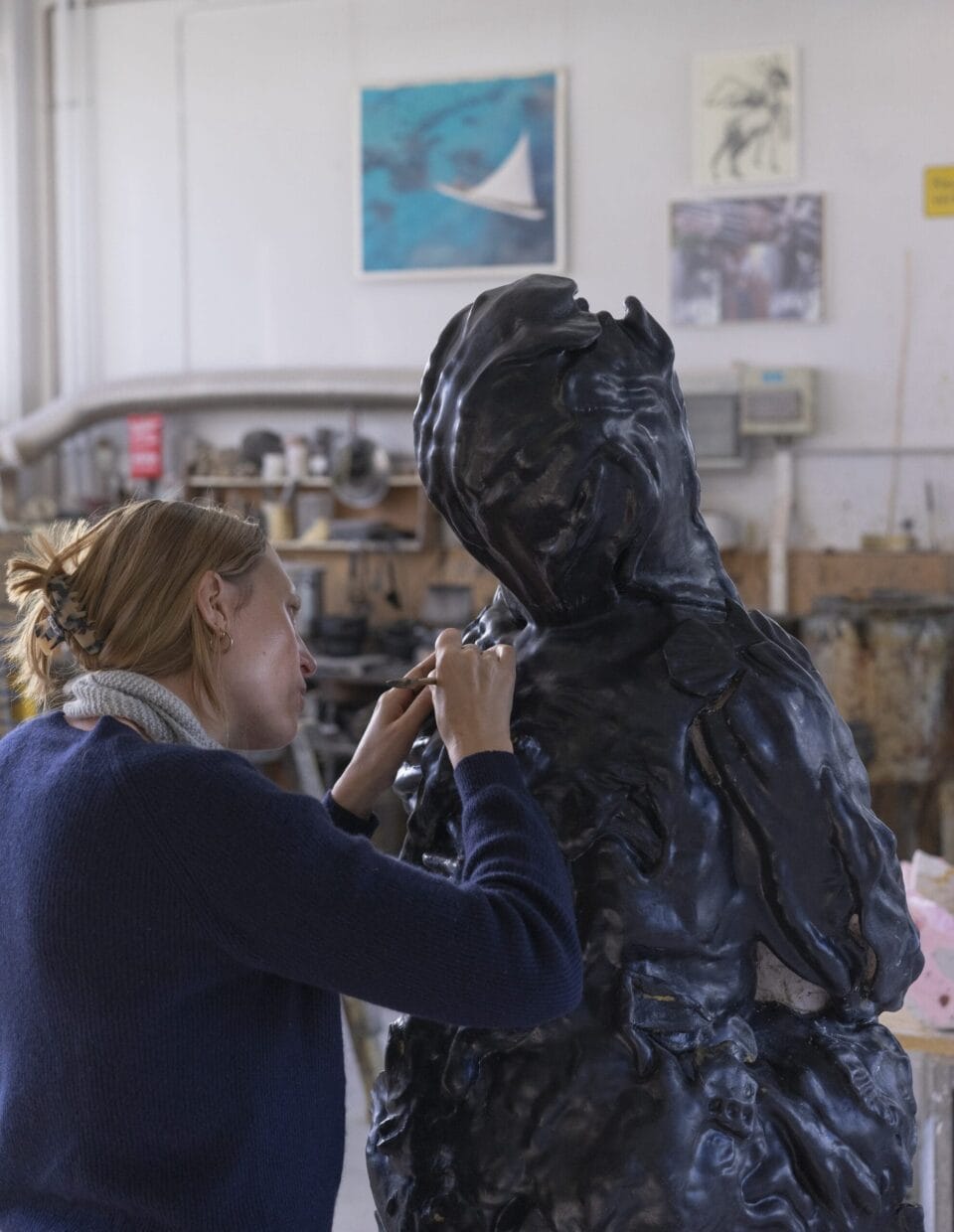 a woman sculpts an elf-like figure in a studio