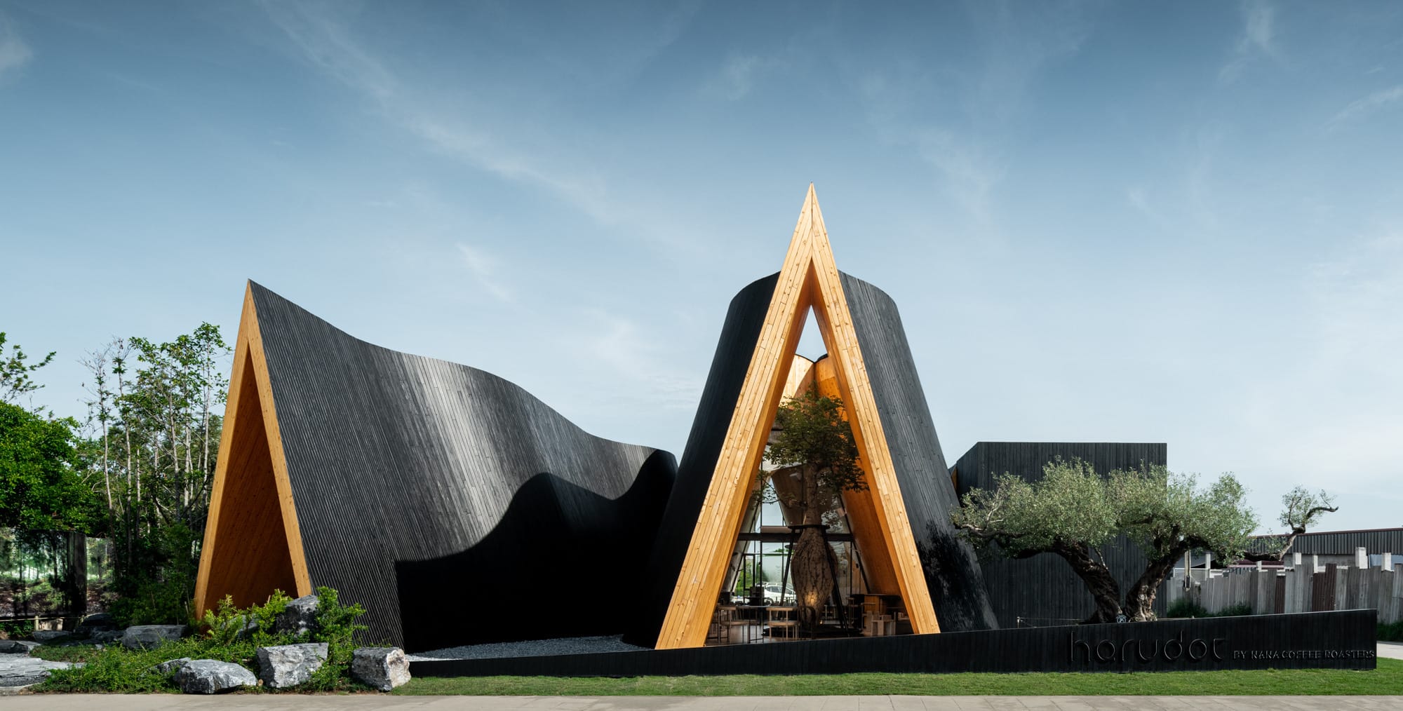 the exterior of a new coffee shop, clad in vertical black timber with two gable ends and undulating sides