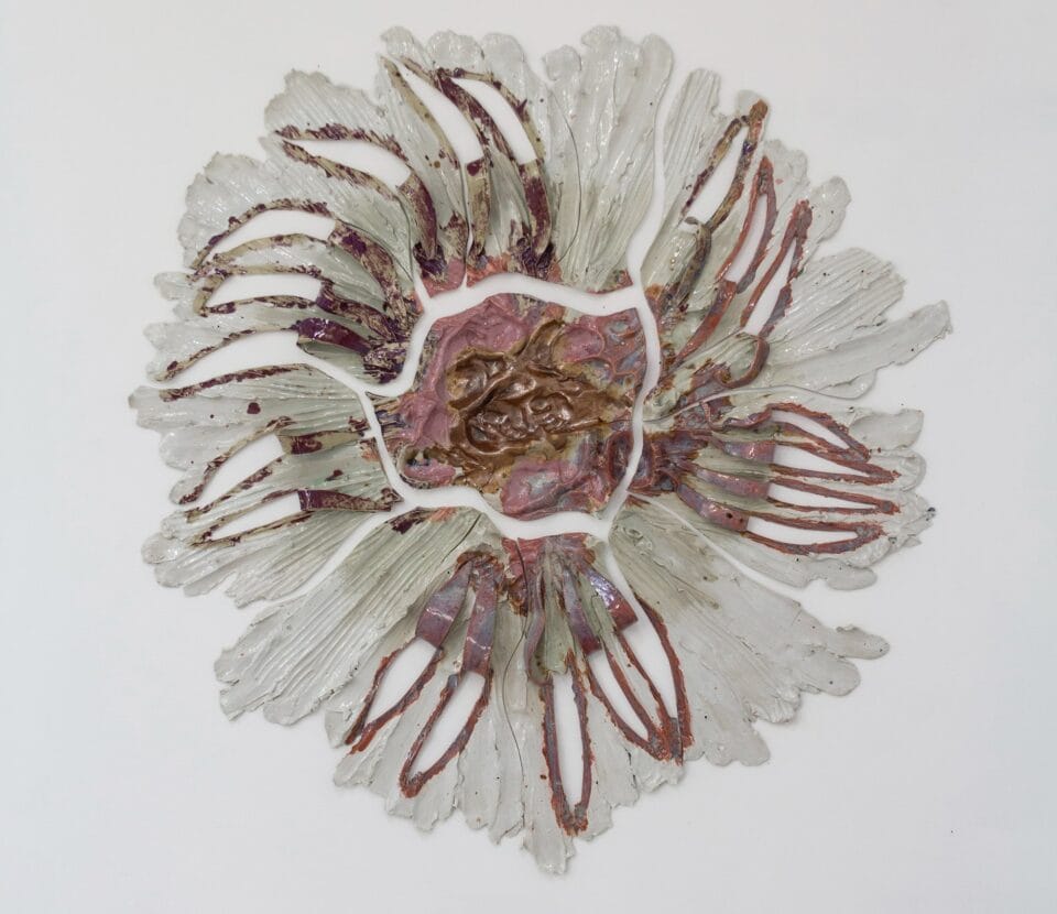 a round pink and white wall sculpture that shows pieces of ceramic with lines evocative of stretching radiating from a central point. 