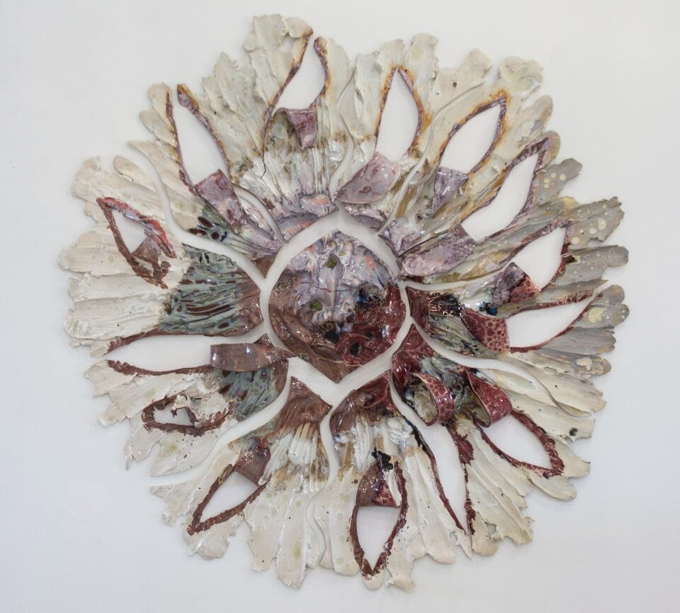 a round pink and white wall sculpture that shows pieces of ceramic with lines evocative of stretching radiating from a central point. 