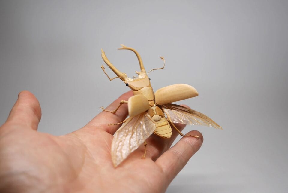 a meticulously detailed wooden sculpture of a horned beetle, photographed in someone's hand