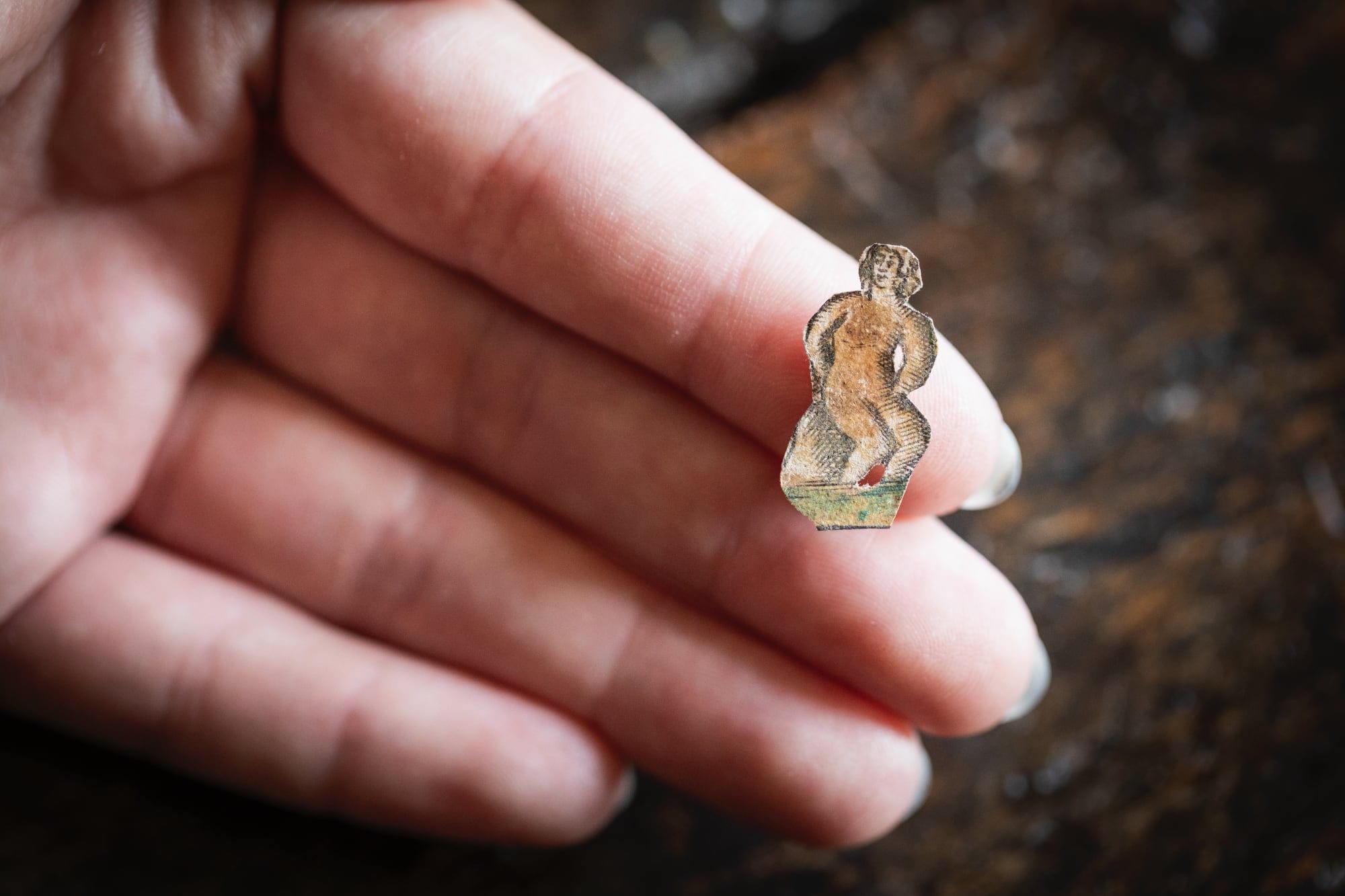 a white hand holding a papercut of a woman on grass