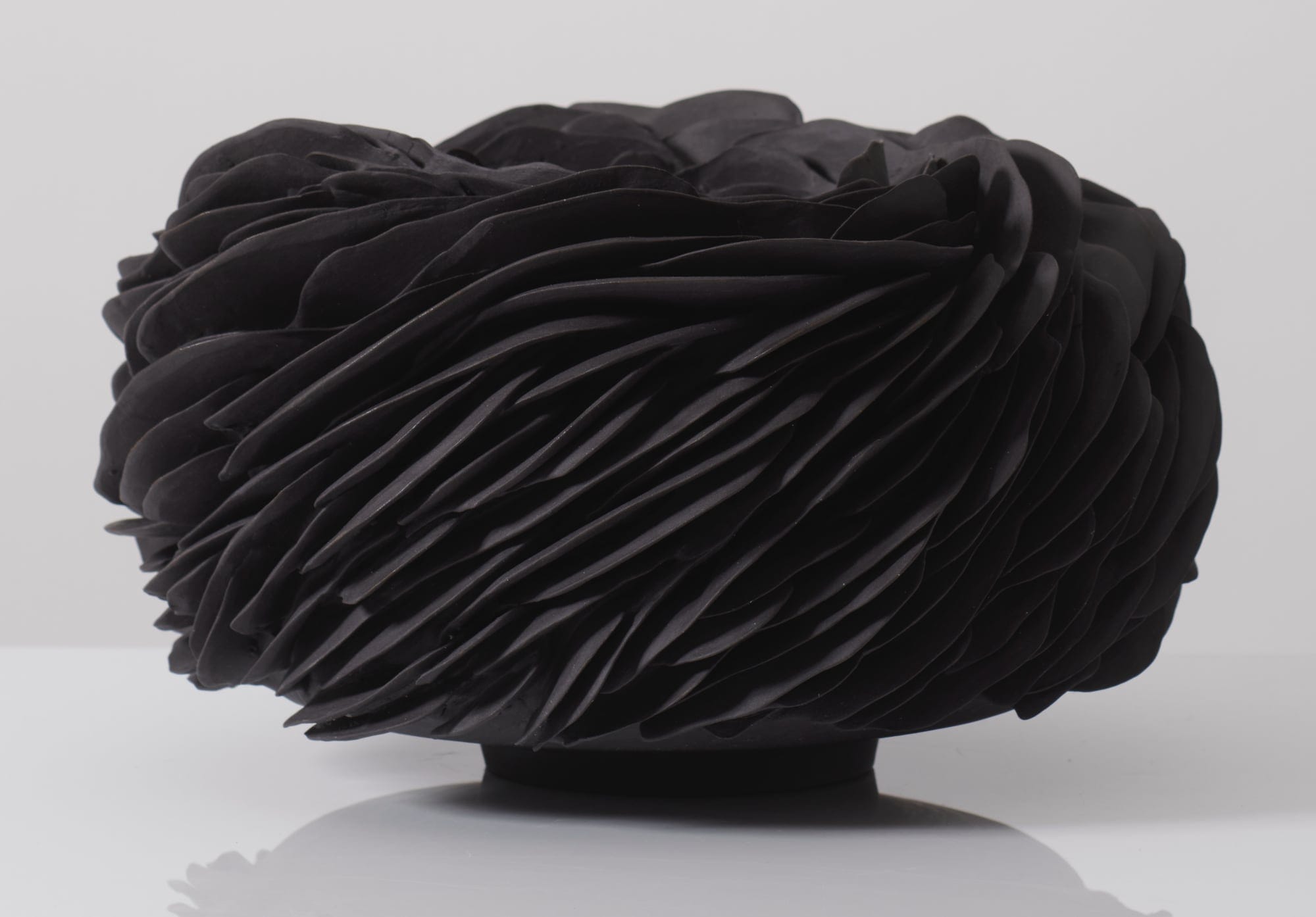 a black porcelain vessel cloaked in innumerable layered fragments